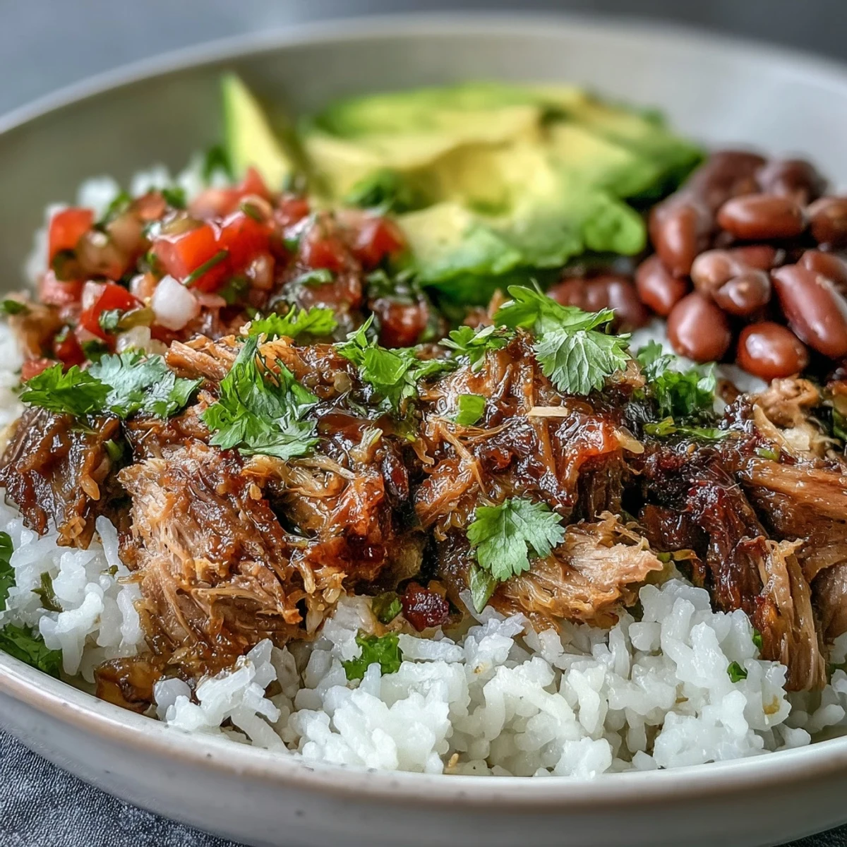 Golden carnitas with crispy edges, fluffy rice, pinto beans, and fresh salsa in a colorful bowl.