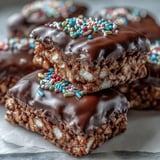 Chocolate Covered Rice Krispy Treats stacked on a white plate, highlighting crunchy cereal and gooey marshmallow layers.  