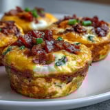 Savory Breakfast Egg Muffins baking in a muffin tin, with fluffy texture and loaded with cheese, onions, and crumbled bacon.
