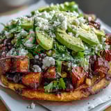 Black Bean and Sweet Potato Tostadas sit on a rustic wooden table, featuring crispy shells topped with roasted orange cubes, black beans, bright avocado slices, and crumbled feta.