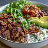 Fresh avocado slices and cilantro garnish a hearty Carnitas Bowl with tender shredded pork.