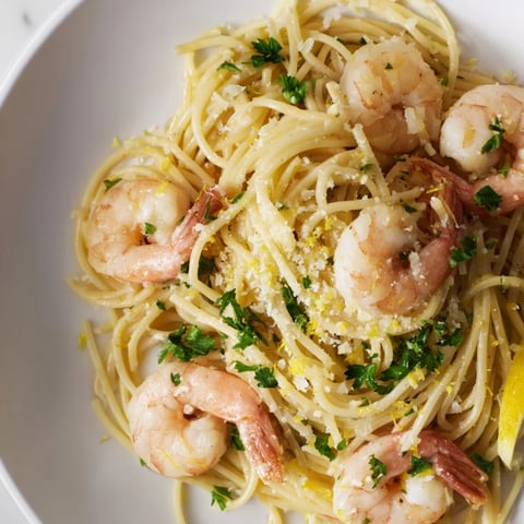 Bright yellow lemon juice glistening on al dente spaghetti with plump sautéed shrimp in a garlic butter sauce, garnished with fresh parsley.