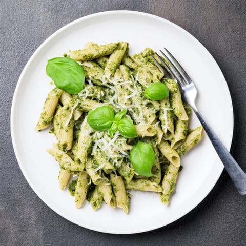 A close-up of creamy sunflower seed pesto pasta in a white bowl, garnished with fresh basil and grated Parmesan cheese.