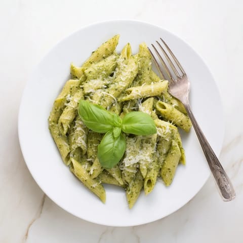 Sunflower seed pesto pasta tossed with penne, vibrant green sauce, and a drizzle of olive oil, served on a rustic wooden table.