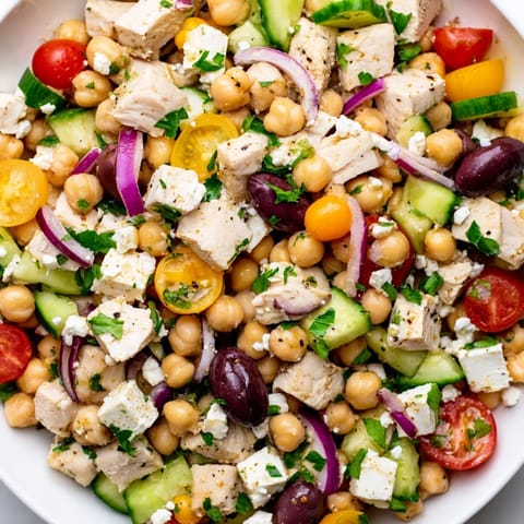Fresh parsley and lemon wedges garnish this vibrant Mediterranean Chickpea Chicken Salad in a white bowl.