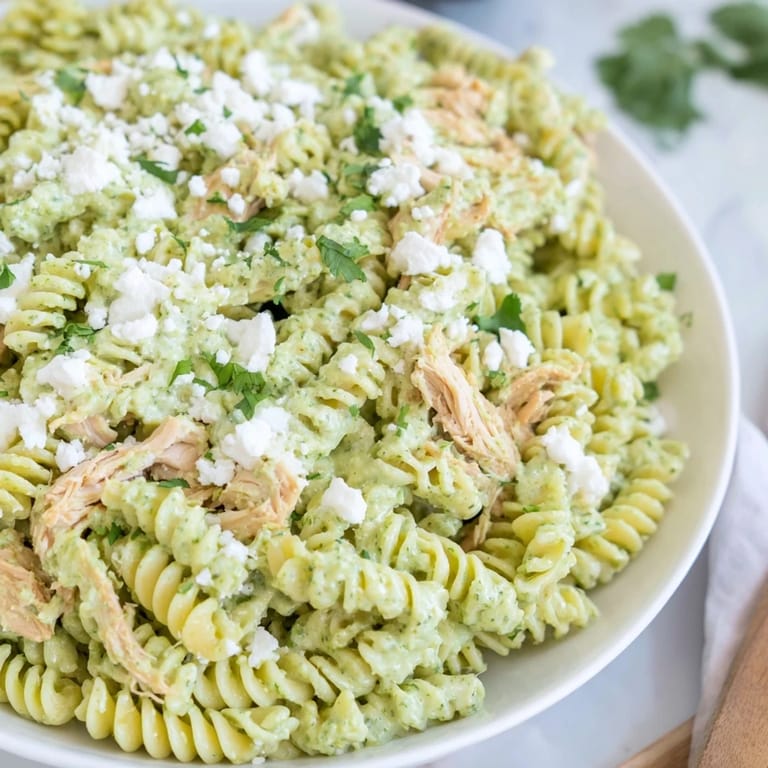A close-up of cilantro lime chicken pasta topped with crumbled feta cheese and fresh herbs.  