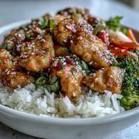 Tender honey garlic chicken glazed in a sweet-savory sauce, served over fluffy rice with crisp broccoli and bell peppers, topped with sesame seeds.